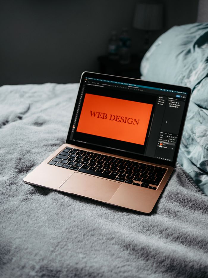 A laptop resting on a bed with web design software displayed, forming a comfortable workspace.